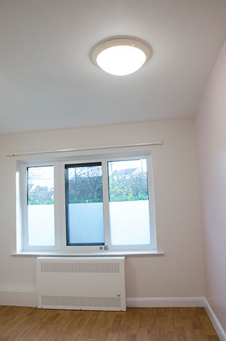A photo of a room with the light on with 3 windows in the background