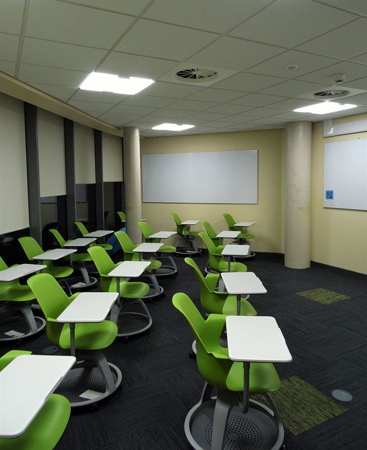 A photo of a classroom with green chairs and white desks attached to the chairs with the lights on
