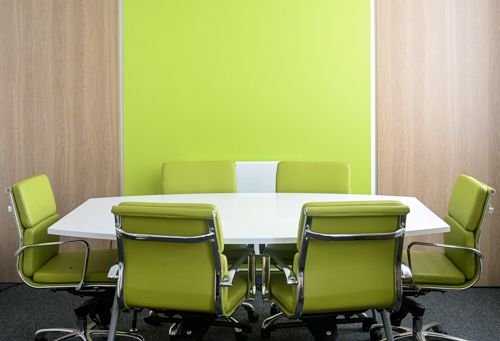 A photo of a meeting room with six green chairs around a table